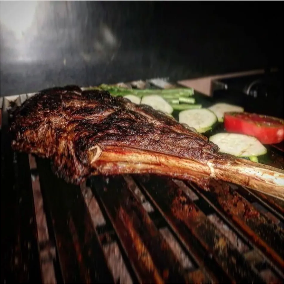 Tomahawk sobre las brasas Tomahawk cocinándose a la parrilla en Brasería en Xàtiva La Patrona